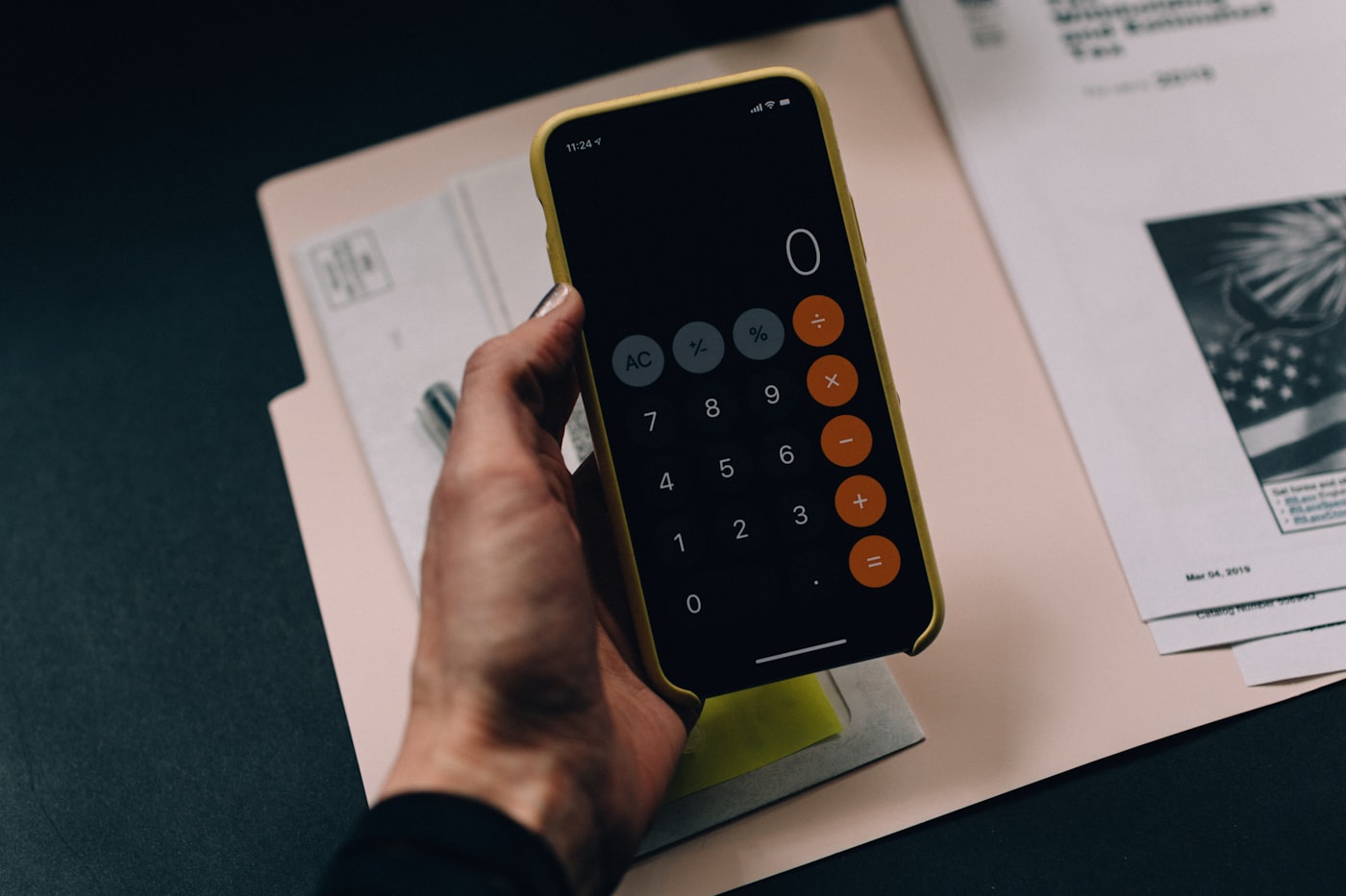 A person holding a phone with a calculator app open, next to paper billing folders
